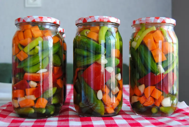 Three jars of assorted pickled vegetables on a red checkered tablecloth