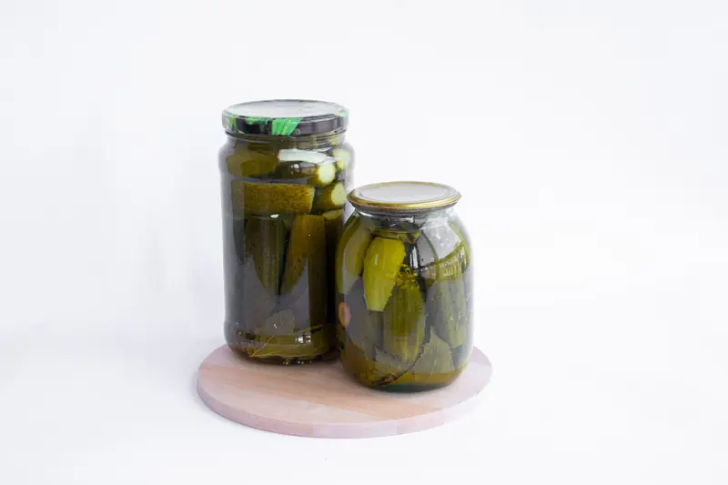 Two jars of pickles sit on a wooden board, showcasing preserved cucumbers in a still life composition