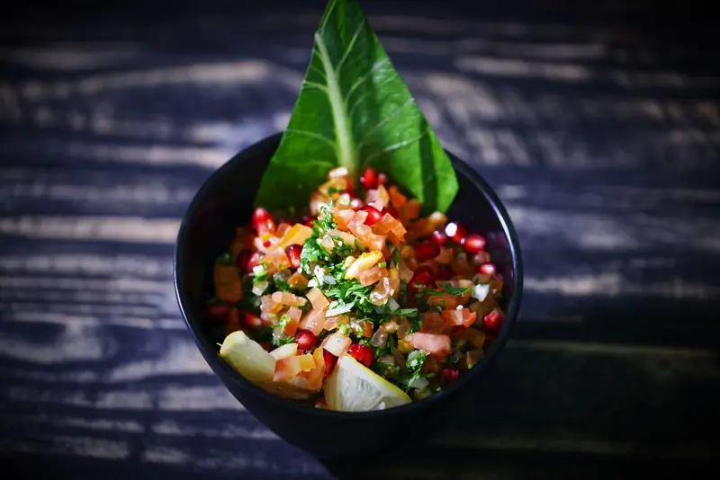 Bright and colorful fresh salsa in a black bowl with a rustic background, featuring pomegranate, tomato, and herbs