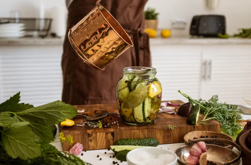 A person preparing homemade pickles using fresh cucumbers and herbs in a rustic kitchen setting