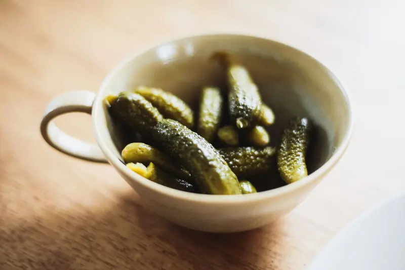 Aesthetic close-up of pickles in a ceramic bowl on a wooden surface