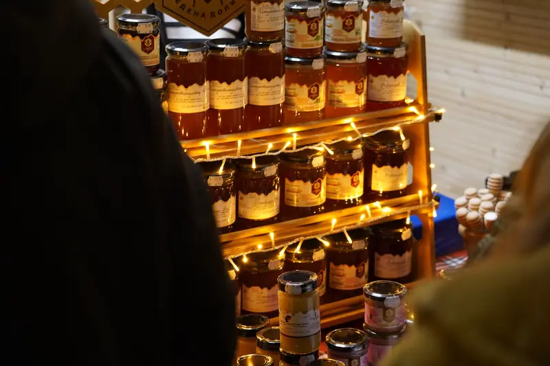 A cozy display of various honey jars lit with warm fairy lights at a market