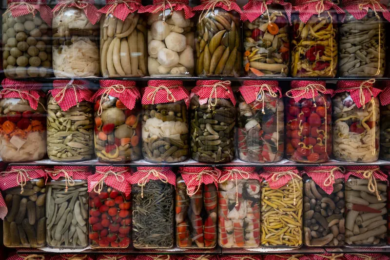 Vibrant assortment of pickled vegetables in jars with red fabric covers, displayed on shelves