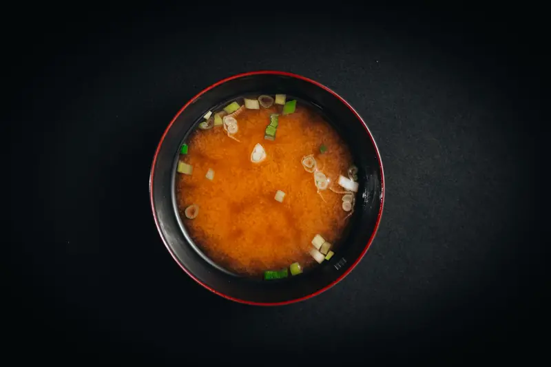 Top view of traditional miso soup with green onions and tofu in a black bowl on a dark background