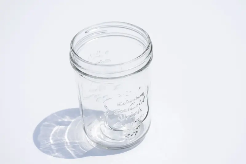 High-angle shot of an empty clear glass jar casting a shadow on a white surface