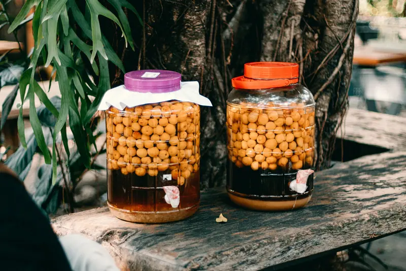 Two jars filled with preserved fruits resting on a rustic outdoor wooden table