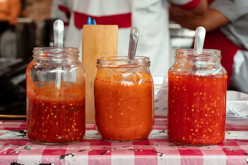 A close-up of three jars filled with vibrant red chili sauces on a red and white checkered tablecloth