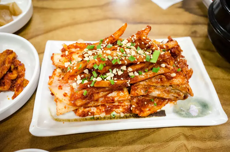 Delicious spicy kimchi served with green onions and nuts on a ceramic plate