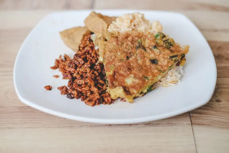 Close-up of vegetarian nasi campur dish on a white plate with tempeh and fritter
