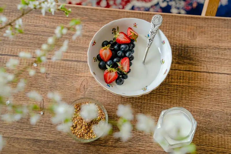 A bowl of fresh strawberries, blueberries with yogurt on a wooden table, viewed from above