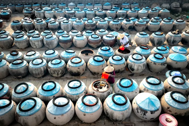 Aerial view of traditional Asian ceramic jars used for fermentation. Two women work in a sunny outdoor setting