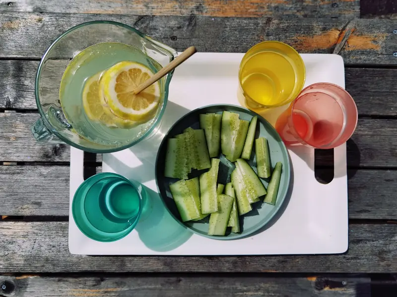 Top view of summer drinks and cucumber slices on a tray outdoors on a wooden table