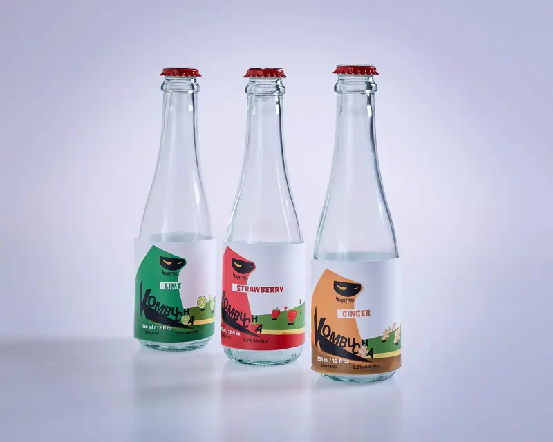 Three labeled kombucha bottles featuring lime, strawberry, and ginger flavors on a white surface