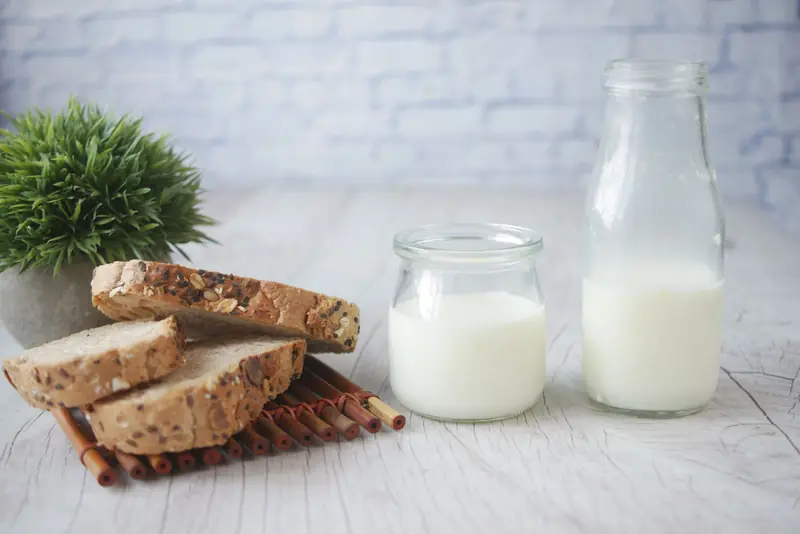Slices of multigrain bread with a bottle and jar of milk on a wooden table