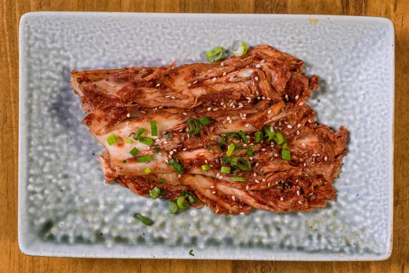 Close-up of fresh homemade kimchi garnished with green onions and sesame seeds on a textured plate