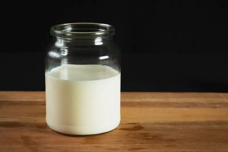 A glass jar filled with milk on a wooden surface against a black background, perfect for dairy-related themes